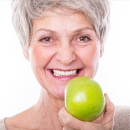 An older woman smiling while holding an apple
