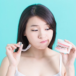Woman looking at Invisalign tray and mouth model with braces